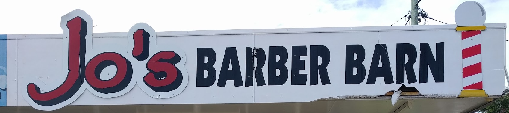 The painted Jo's Barber Barn fascia sign, with a barber pole at the end